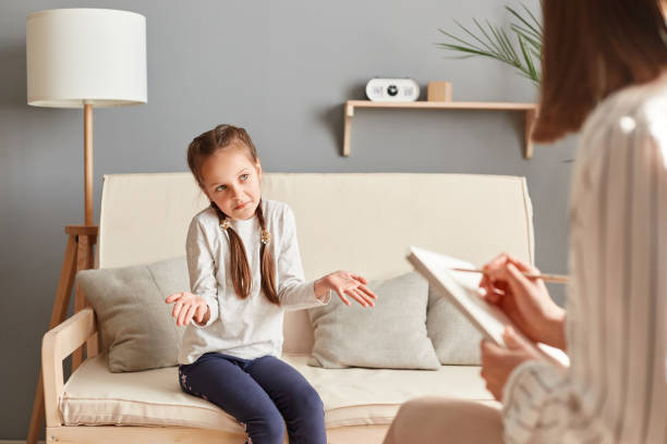 istock Unrecognizable female psychologist providing mental therapy for uncertain confused little girl in her office, taking notes on the girl's condition and progress during the session. 1488507607