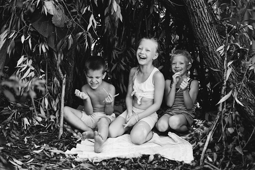 Three children play in a hut which they themselves have built from leaves and twigs. Black and white photography