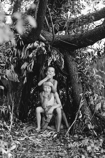 Three children play in a hut which they themselves have built from leaves and twigs. Black and white photography