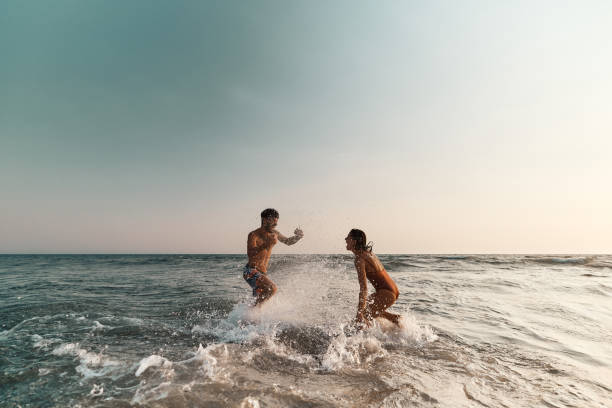 Cheerful couple having fun while splashing each other at sea. stock photo