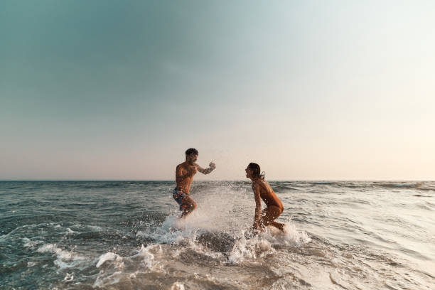 Casal alegre se divertindo enquanto espirra um ao outro no mar. - foto de acervo