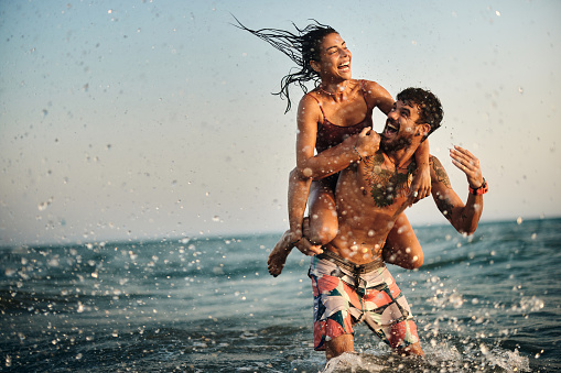 Cheerful couple having fun while piggybacking in summer day at sea. Copy space.