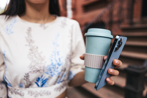 Close up of a busy woman holding mobile phone and a coffee cup in New York City.