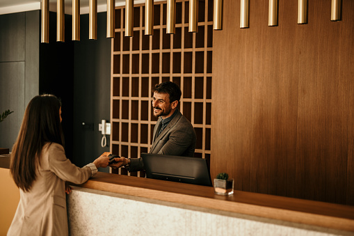 Smiling receptionist behind the hotel counter attending to a female guest. The concierge gives the documents to hotel guest.