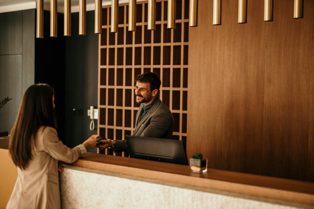 Smiling receptionist behind the hotel counter attending to a female guest. The concierge gives the documents to hotel guest. stock photo