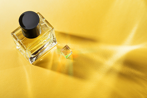 Transparent bottle of perfume on a yellow background with sun light caustic rays.