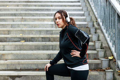 Young sportswoman resting with hands on knees at bottom of stairs. Sport, fitness and wellness concept