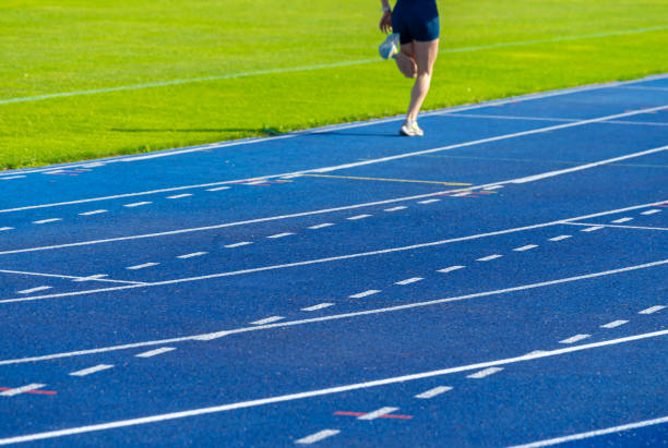 Young male athlete in a white shirt preparing for a race on a red running track.