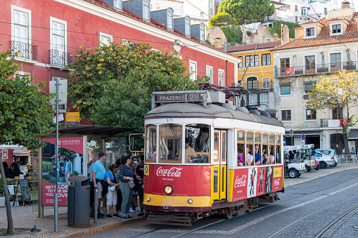 Lisbon, Portugal-October 2022: Close up view of a red colored tramcar at a stop with passengers waiting to board  in the Alfama neighborhood