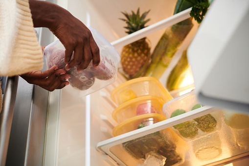 Woman putting container with fresh fruits in refrigerator