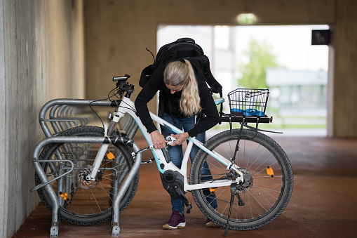 one mature adult woman with long hair locking her electric bike at bicycle parking at railroad station