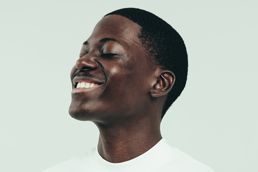 Happy young man celebrating his beautiful and glowing melanin skin with a smile. Youthful black male showing off the radiance he has achieved from a healthy skincare and grooming routine.