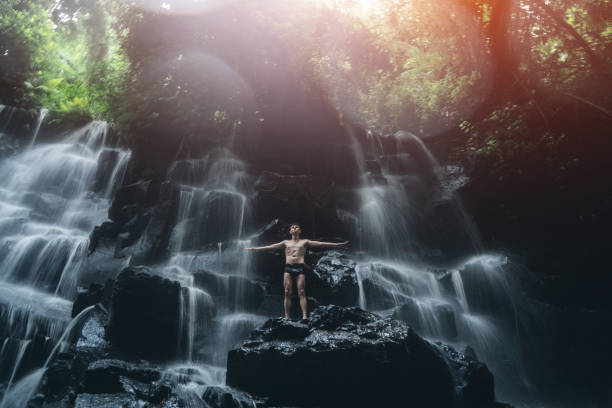 male standing at waterfall in bali indonesia - bali male beautiful ethnicity imagens e fotografias de stock