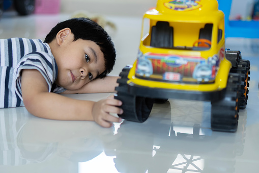 Childhood, kids and people concept - lovely Asian baby boy playing with yellow toy car on floor at home.