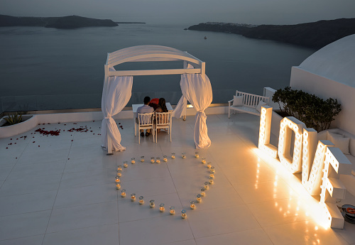 Imerovigli, Santorini, Greece - July 1, 2021: On a romantic evening, a couple admires the sunset in Santorini from the terrace