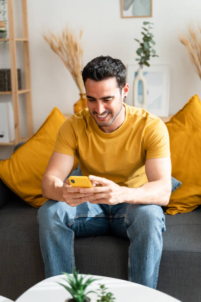 istock Man using mobile phone sitting on living room sofa. 1488536380