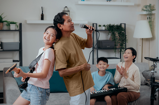 Asian Grandfather enjoy singing and playing music with family in the living room at home