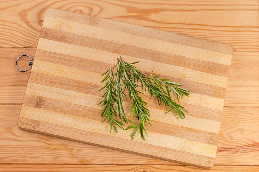Twigs of the fresh rosemary on a bamboo wooden cutting board on the rustic table