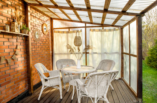 istock Boho style home patio terrace with curtains and wicker, rattan, reed decorations. Wall made with greenhouse plastic and ceiling is polycarbonate. White garden furniture, mirrors red on brick wall. 1488537661