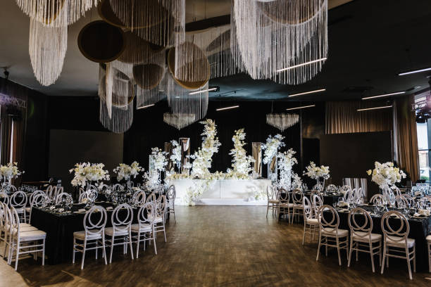 Festive tables with flower composition on black tablecloth and chairs for guests. Wedding set up, dinner table reception in area on party. Banquet decoration in hall restaurant. Setting. Side view.