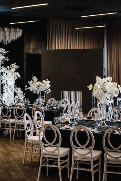 istock Festive tables with flower composition on black tablecloth and chairs for guests. Wedding set up, dinner table reception in area on party. Banquet decoration in hall restaurant. Setting. Side view. 1488540563