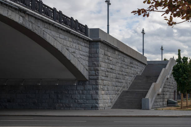 Side view of grey stone stairway to bridge located above city street road in cloudy day. No people. Soft focus. General architecture theme.