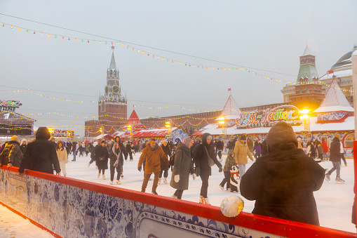 Russia, Moscow - January 03, 2023: Happy people slides on ice rink of Christmas market on Red square by Moscow kremlin. Soft focus. Winter holidays in Russia theme.