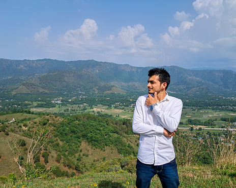 Young man standing outdoor in summer mountains at day time and enjoying view of nature. Mandi, Himachal pradesh, India