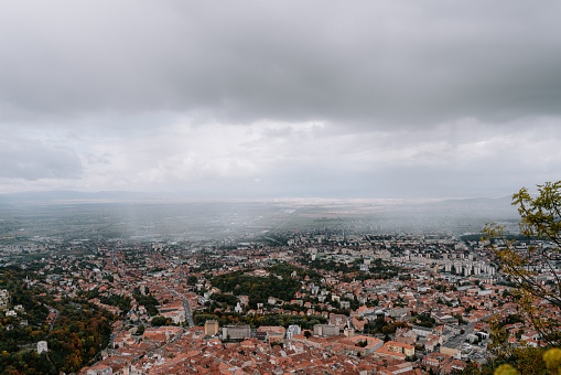 An aerial shot of the cityscape of Brasov, Romania under a cloudy sky.