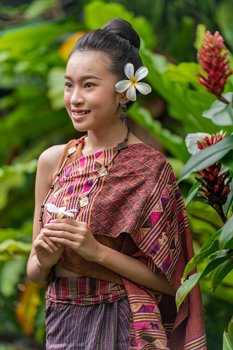 Half body shot of a young and beautiful Lao women wearing traditional Laos costume outside a lush tropical park