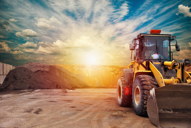 Heavy equipment machine wheel loader on construction site . Precast and concrete industry A excavator moves along a road in an industrial landscape, the sky filled with clouds above it. A symbol of transportation and machinery building sand stock pictures, royalty-free photos & images