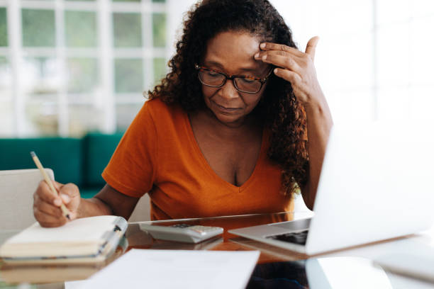 Retired woman getting stressed while doing her personal budget Female pensioner showing signs of stress while managing her personal budget, struggling to make ends meet. Senior woman sitting in her home office, wearing an expression of frustration and worry. financial item stock pictures, royalty-free photos & images