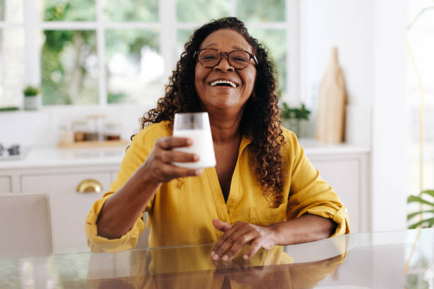 donna anziana felice che beve latte come parte di una dieta sana - 60s senior adult breakfast cheerful foto e immagini stock