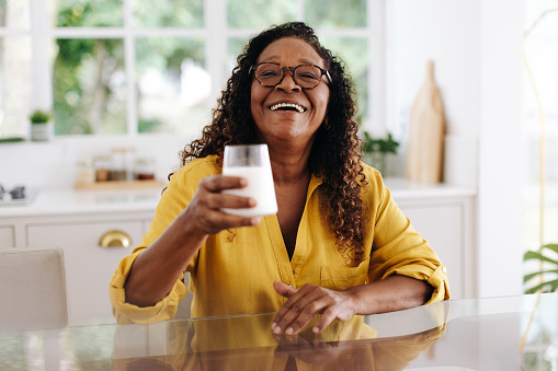 Happy senior woman drinking fresh milk to get calcium and other nutrients that support bone health and overall wellness. Mature black woman enjoying a dairy product in her diet at home.