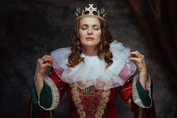 medieval queen in red dress with white collar and crown on dark gray background.