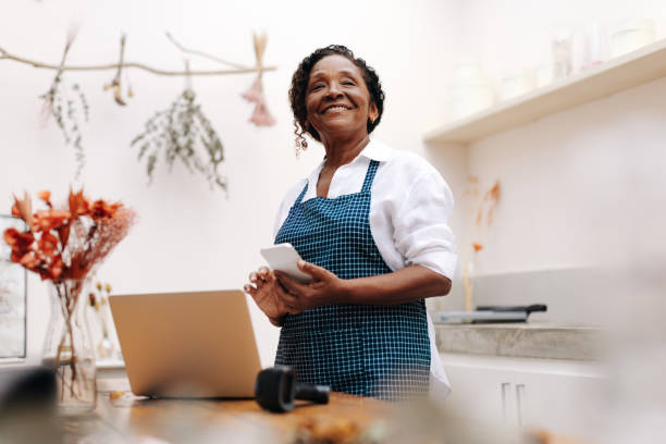 feliz mujer de negocios sosteniendo un teléfono inteligente en su floristería - florist telephone flower business fotografías e imágenes de stock