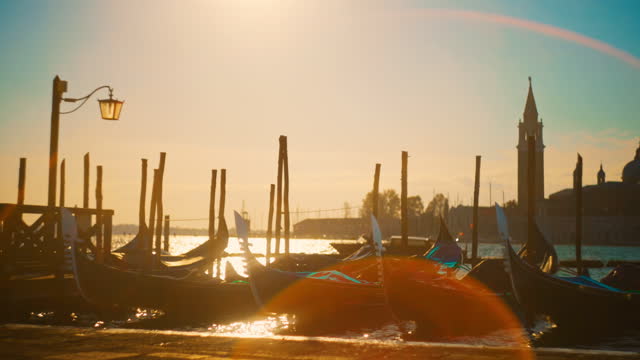 Slow motion Retro Style of gondolas at jetty against sky. Boats moored at canal during sunset. Sunlight reflecting on water.