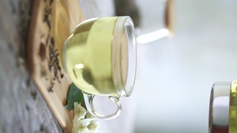 Jasmine tea flows into a glass cup. Jasmine green tea is poured from a glass teapot into a cup