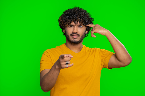You are crazy, out of mind. Displeased indian man pointing at camera and showing stupid gesture, blaming some idiot for insane plan, abuse, bullying. Hindu guy isolated on green chroma key background