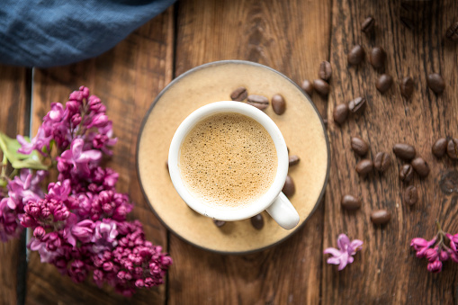Coffee composition with cup of natural coffee and coffee beans on beige background with pink flowers and copy space.