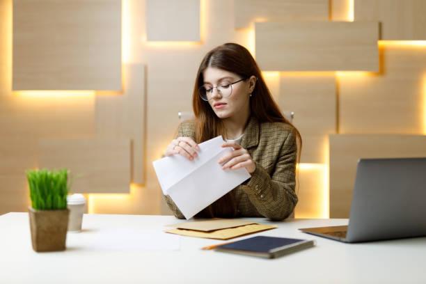 young businesswoman in glasses looks through paper mail and bills at the workplace in the office. - news of the world imagens e fotografias de stock