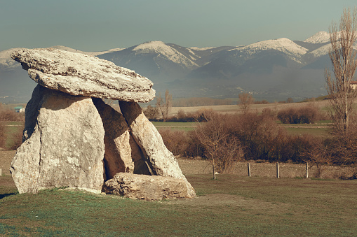 Dolmen in the green plain under the snowy mountains in a clear an d sunny day of winter