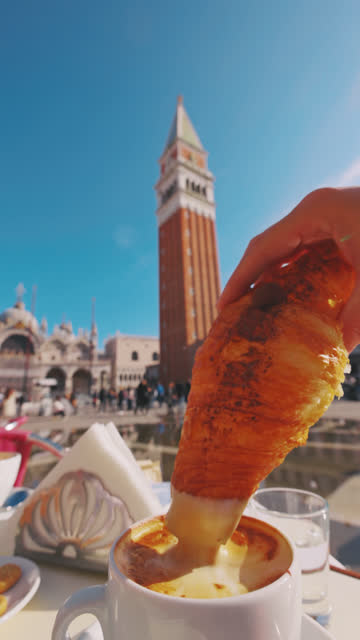 Slow motion of woman dipping croissant in coffee. Tourist is having food at sidewalk cafe. She is at St Mark's Square.