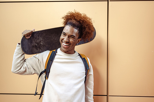 Urban young African American man holding a skateboard and looking aaway