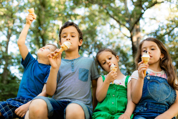 Ice cream , sweet child's refresment Group of children sitting in a row and eating ice cream cone in nature licking ice cream cone stock pictures, royalty-free photos & images