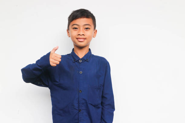Smiling confident boy wearing a blue casual shirt looking at the camera with showing thumb up isolated on white background Smiling confident boy wearing a blue casual shirt looking at the camera with showing thumb up isolated on white background child 10 11 years 8 9 years cheerful stock pictures, royalty-free photos & images