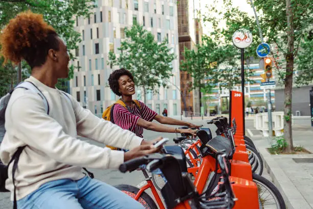 Cheerful African American young people in urban part of the city. They are using public bicycles in the city