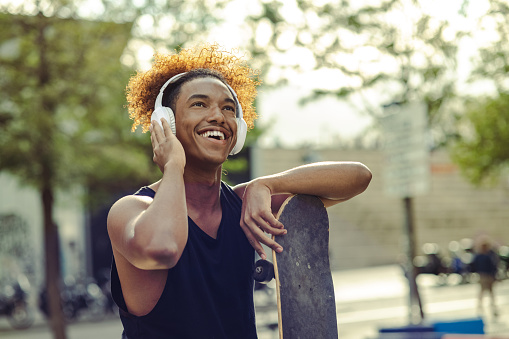 Shot of a young man holding a skateboard outside and listening to music