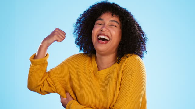 Wink, arm and bicep with a black woman joking in studio on a blue background for fun or humor. Playful, strong and muscle with an attractive young female comic flexing while winking or laughing