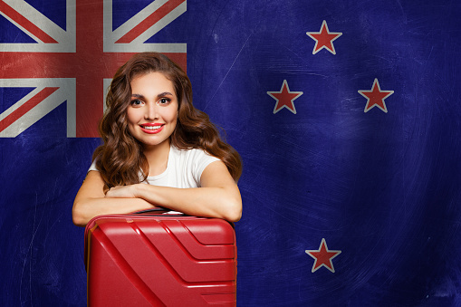 Travel in New Zealand concept. Happy woman with suitcase on flag of New Zeland. Welcome to New Zeland